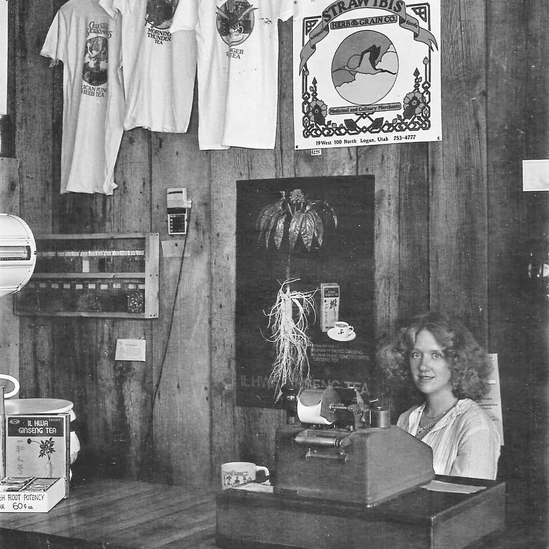 Old image of Caffe Ibis founder, Sally, sitting at counter of original "Straw Ibis Herb & Grain Company - Medicinal and Culinary Merchants."