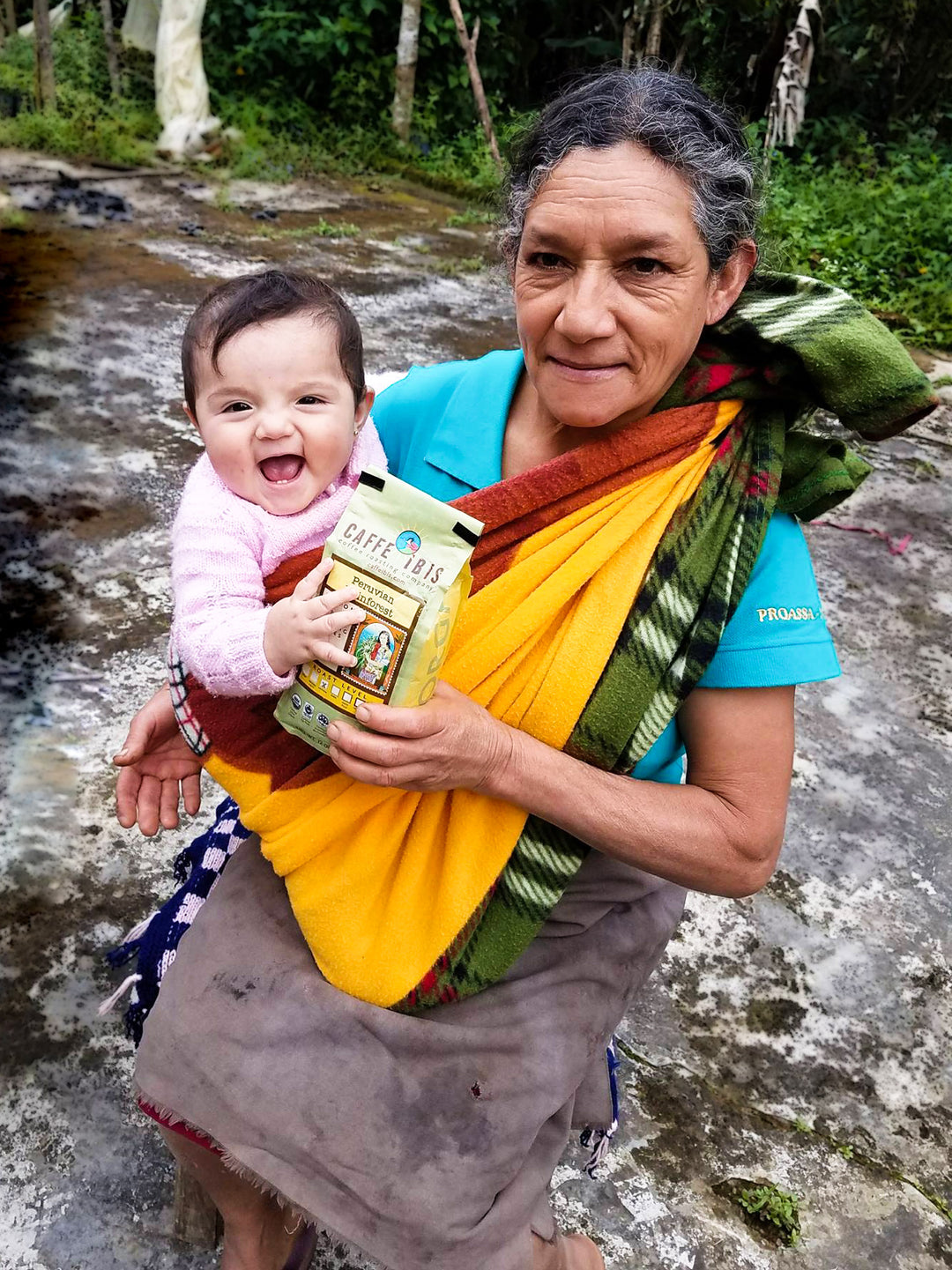 Image of peruvian coffee producer holding a baby and 12oz bag of Caffe Ibis Peruvian Rainforest coffee.
