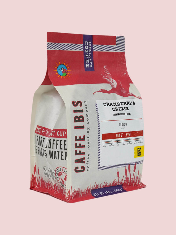 Caffe Ibis flavored Cranberry and Creme coffee in a pink twelve ounce bag; front quarter view.