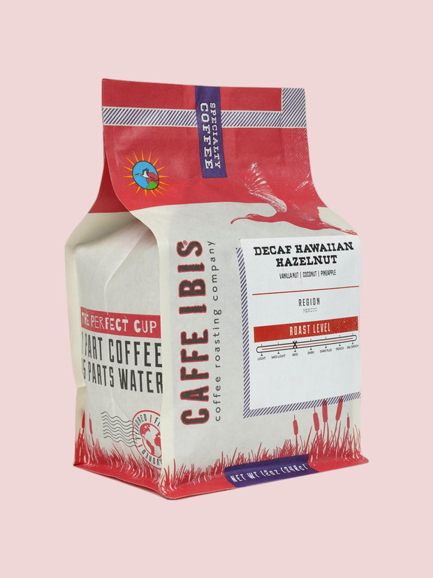Caffe Ibis Decaf Hawaiian Hazelnut flavored coffee in a pink twelve ounce bag; front quarter view.