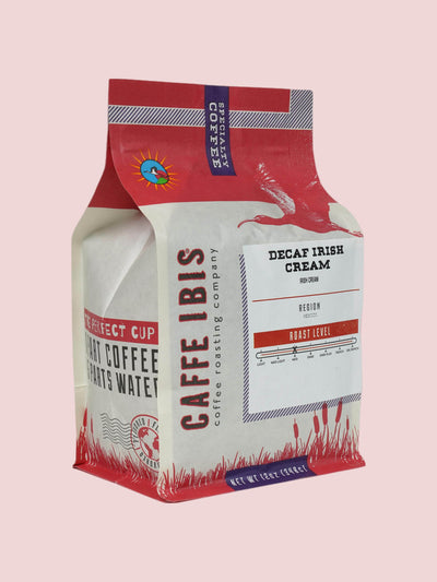 Caffe Ibis Decaf Irish Cream flavored coffee in a pink twelve ounce bag; front quarter view.